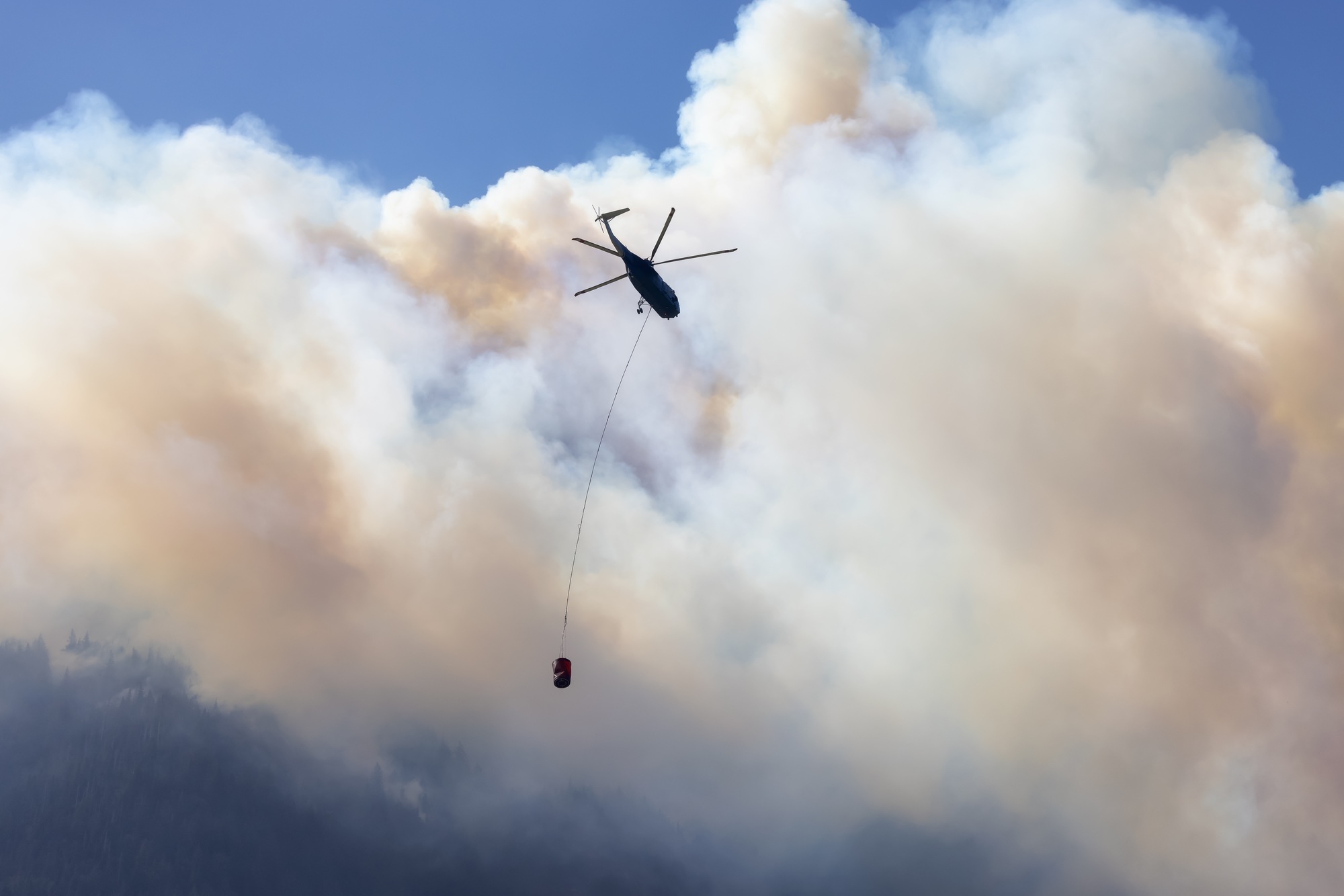 Wildfire Service Helicopter flying over BC Forest Fire and Smoke on the mountain near Hope